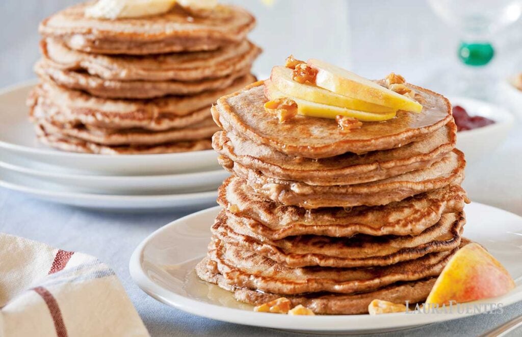 two plates with stacks of whole wheat pancakes topped with sliced apples