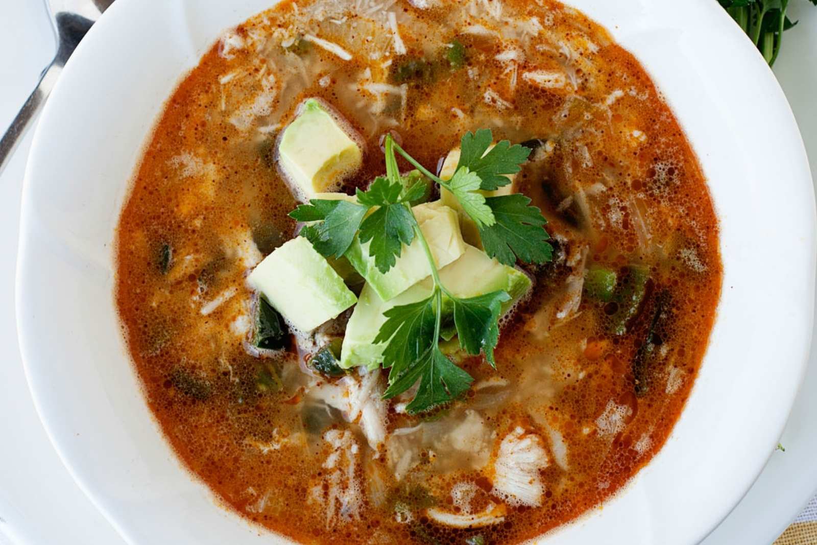 overhead view of spicy chicken chili in a bowl topped with avocado cubes