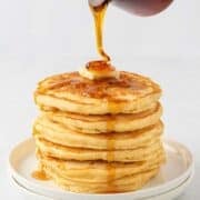 a stack of pancakes being drizzled with syrup