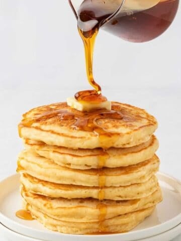 a stack of pancakes being drizzled with syrup