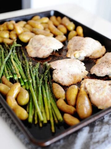 boneless skinless chicken thighs with small potatoes and asparagus in a baking sheet