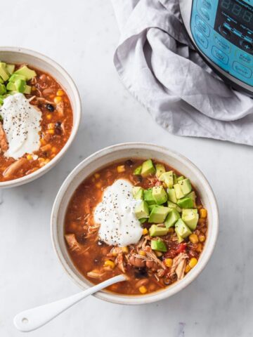 two bowls of a chicken taco soup topped sour cream and avocado next to an instant pot