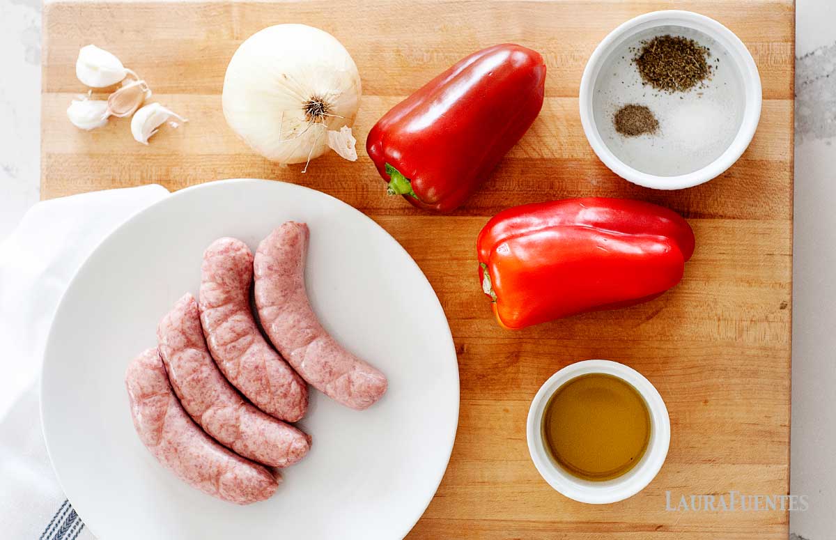 Ingredients for Sausage and Peppers on a cutting board: sausages, peppers, onion, garlic coves, salt, pepper & spices