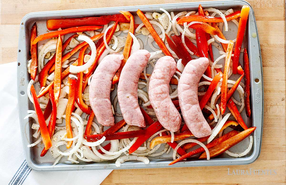 sausages and sliced peppers on a sheet pan prior to baking