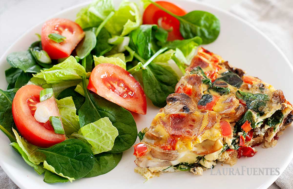 a slice of spinach and bacon frittata on a plate with salad on the side