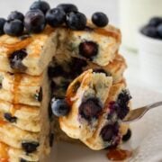 stack of blueberry pancakes with one bite cut out of them on a fork