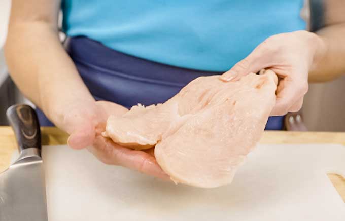 woman holding butterflied chicken breast up to camera