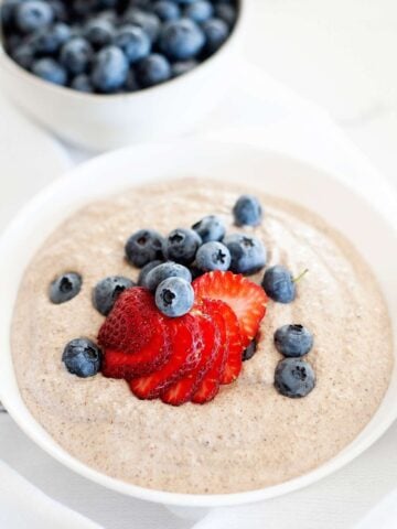 bowl of paleo oatmeal with berries on top, and a small bowl of bluberries behind