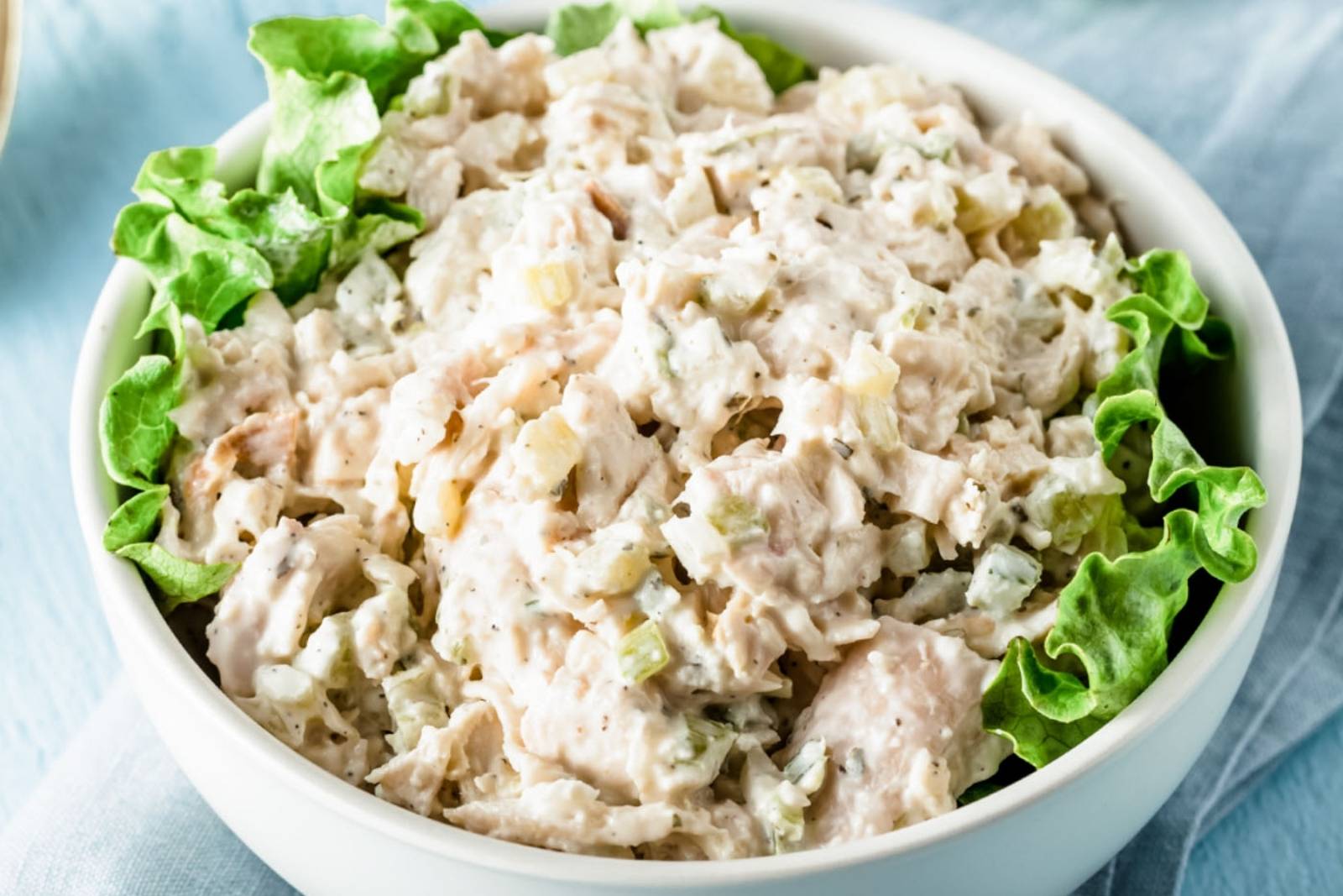 a bowl of chicken salad eith lettuce leaves on the sides