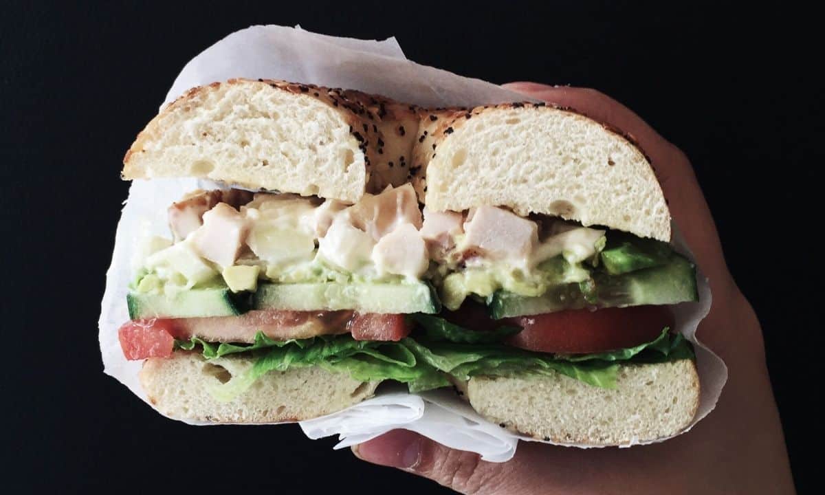 a hand holding a sandwich filled with chicken salad and veggies
