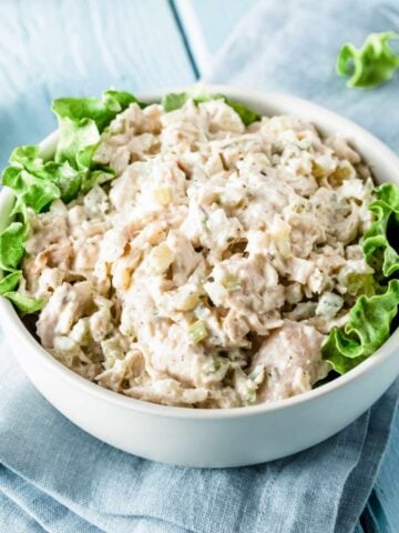 a bowl of chicken salad eith lettuce leaves on the sides