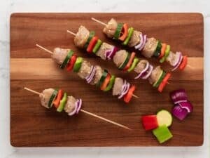 assembling chicken and veggie kabobs in wooden skewers on a wooden board