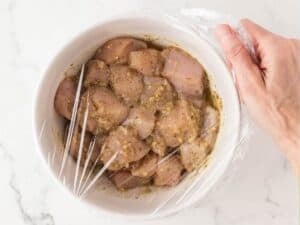 bowl of chicken cubes tossed in a kabob marinade covered with plastic wrap ready to marinade