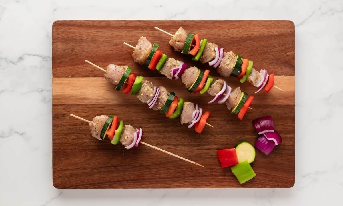 assembling chicken and veggie kabobs in wooden skewers