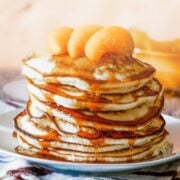 Fluffy stack of peach pancakes topped with peaches and pancake syrup on a plate