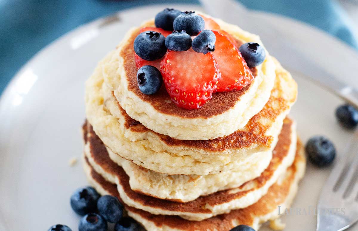 stack of almond flour pancakes topped with strawberries and blueberries