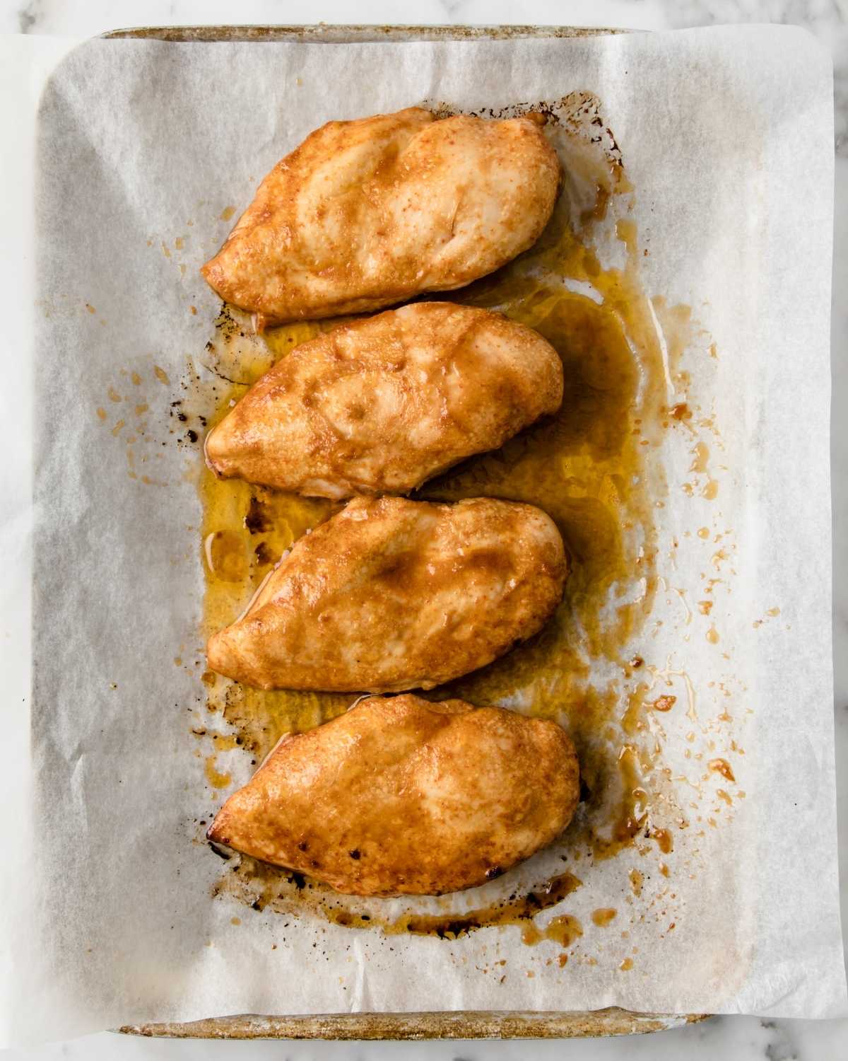 four baked chicken breasts on a baking sheet