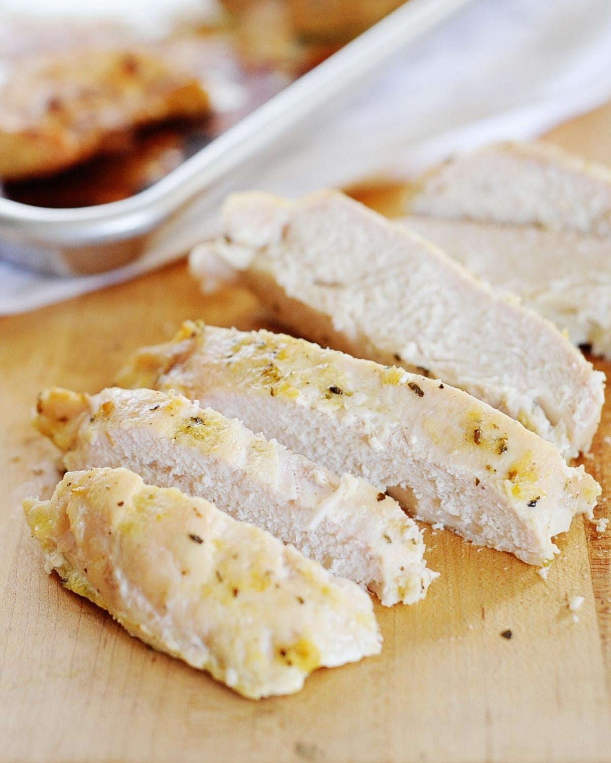 sliced chicken breast on a cutting boar with a baking sheet in the background