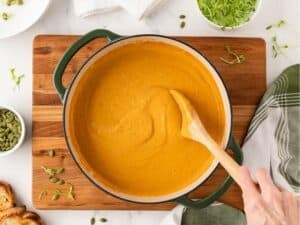 stirring acorn squash soup in a pot after it's been blended smooth