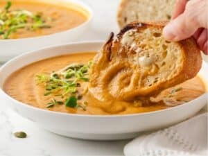 dipping a slice of crusty bread into a bowl filled with acorn squash soup