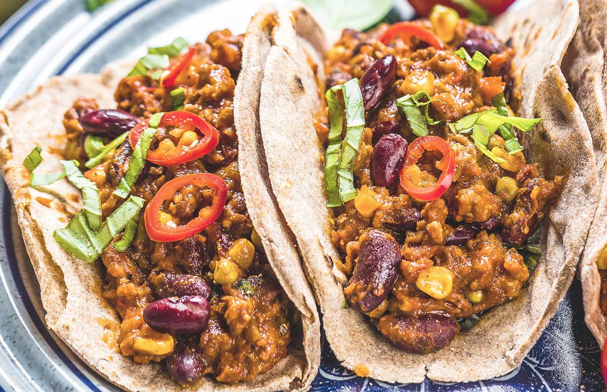 two chili tacos topped with red peppers and shredded lettuce