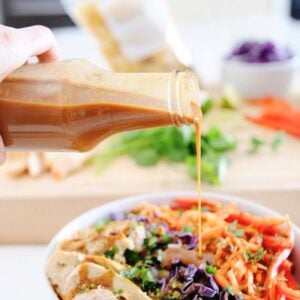 bottle filled with homemade thai peanut dressing being poured over a salad