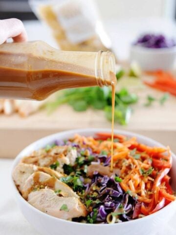 bottle filled with homemade thai peanut dressing being poured over a salad