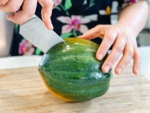 woman slicing a whole acorn squash on a wooden board while holding it with her hand