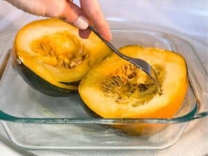 two acorn squash halves in the microwave being poke with a fork