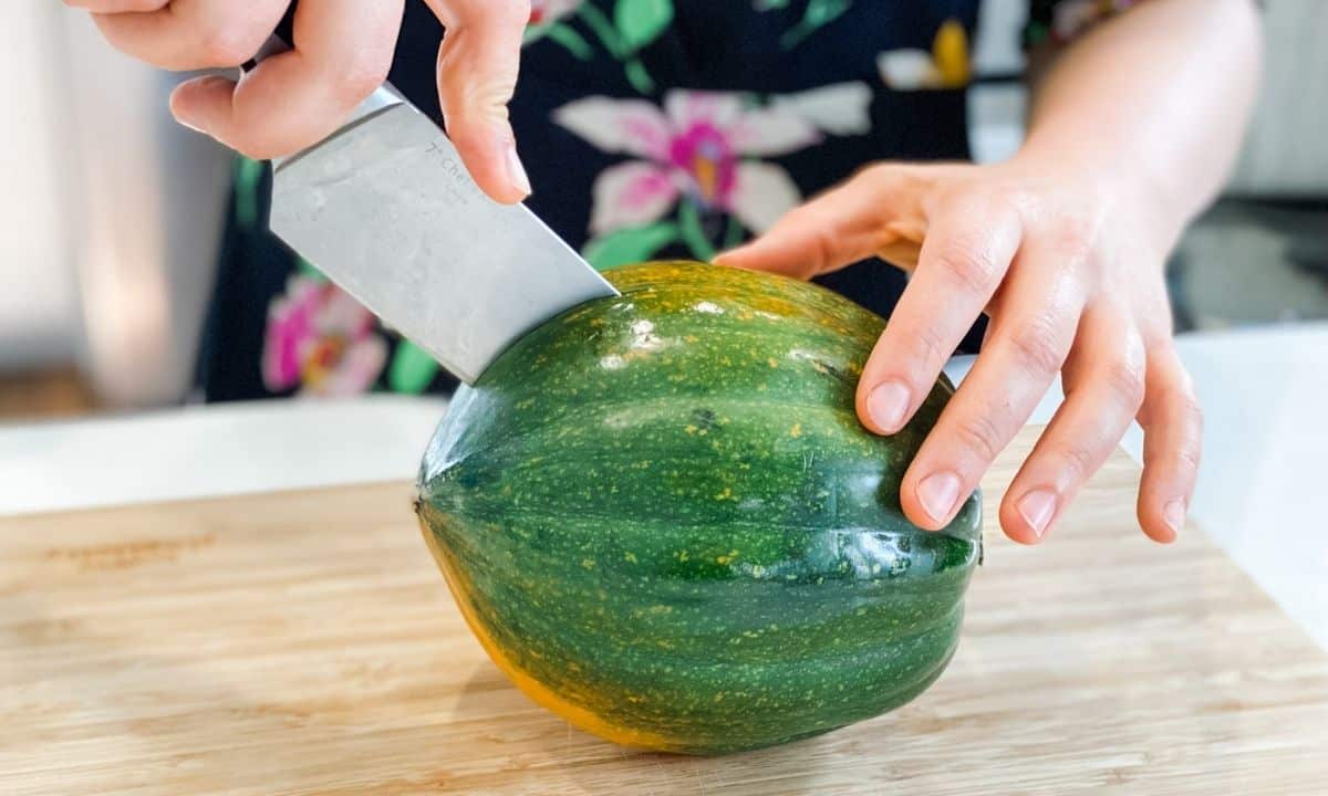 woman slicing a whole acorn squash on a wooden board while holding it with her hand