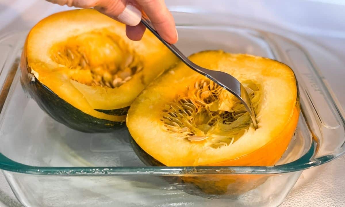 two acorn squash halves in the microwave being poke with a fork