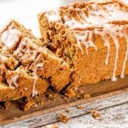 Paleo pumpkin bread topped with a glaze, sliced on a wooden cutting board