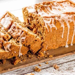 Paleo pumpkin bread topped with a glaze, sliced on a wooden cutting board