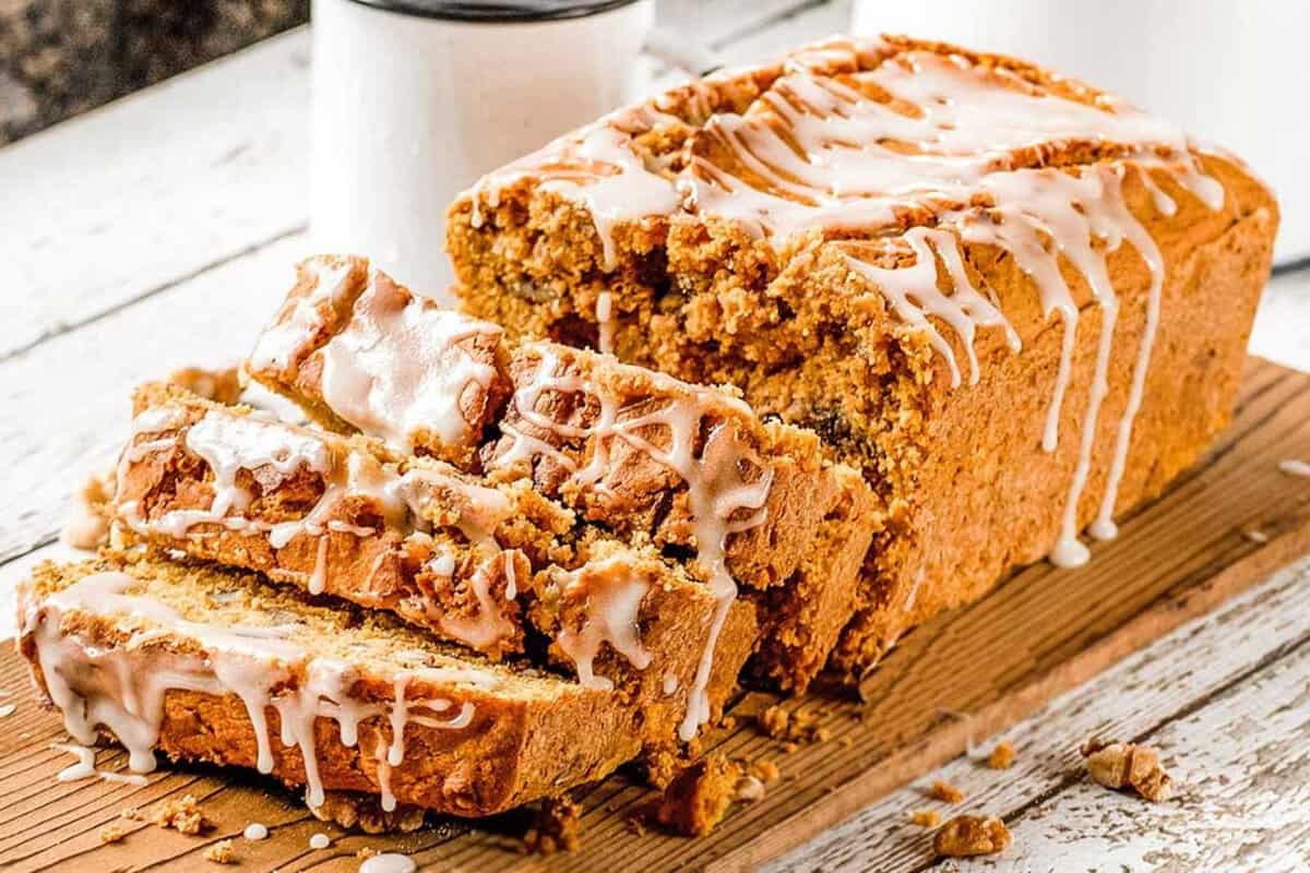 Paleo pumpkin bread topped with a glaze, sliced on a wooden cutting board