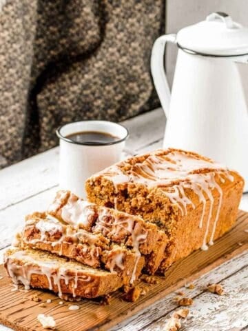 Paleo pumpkin bread topped with a glaze, sliced on a wooden cutting board and served with a cup of coffee and a white enamel coffee kettle.