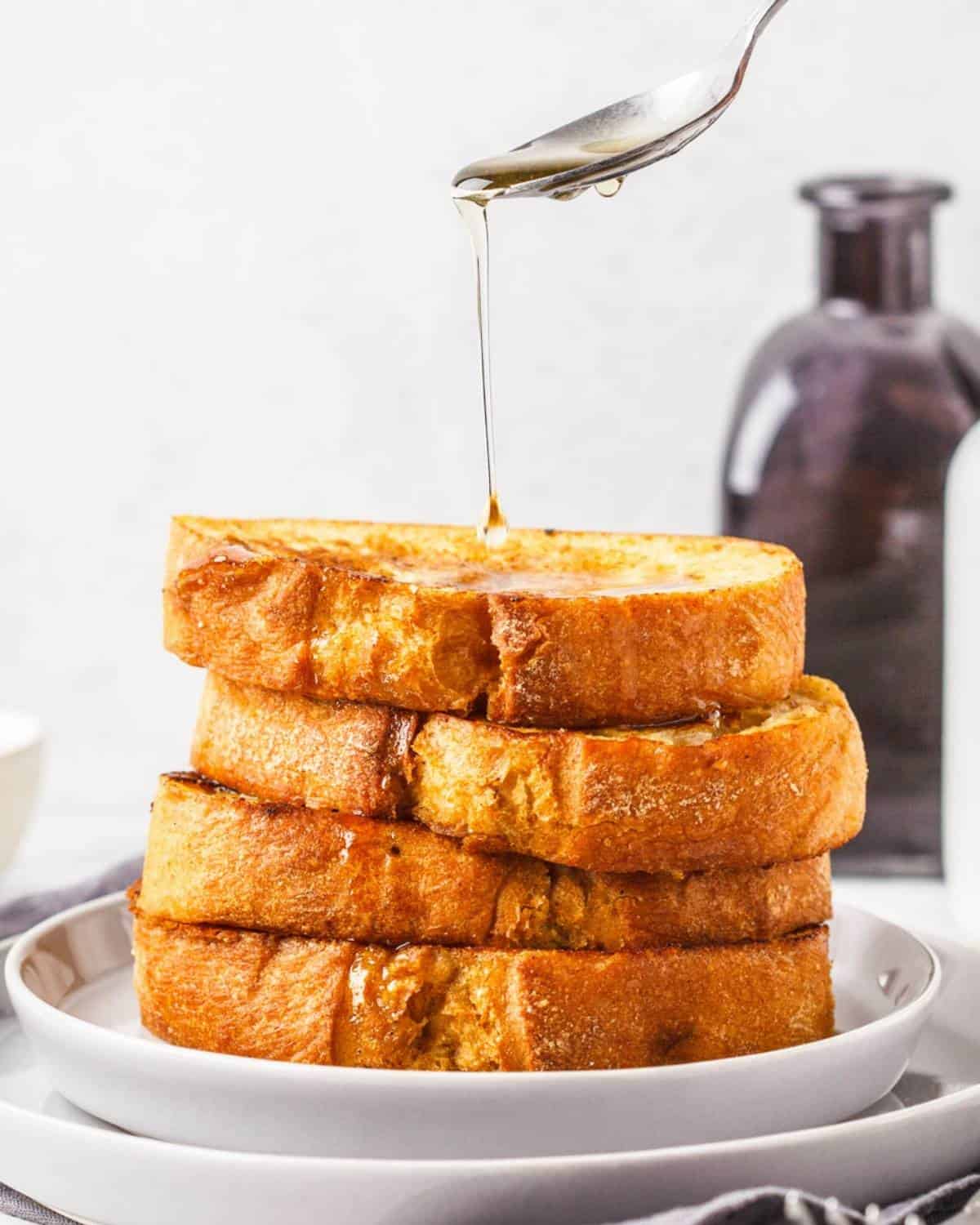 syrup being poured over a stack of four thick pumpkin French toast slices