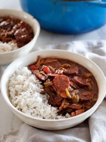 two bowls of chicken gumbo with white rice, and a blue soup pot on the back