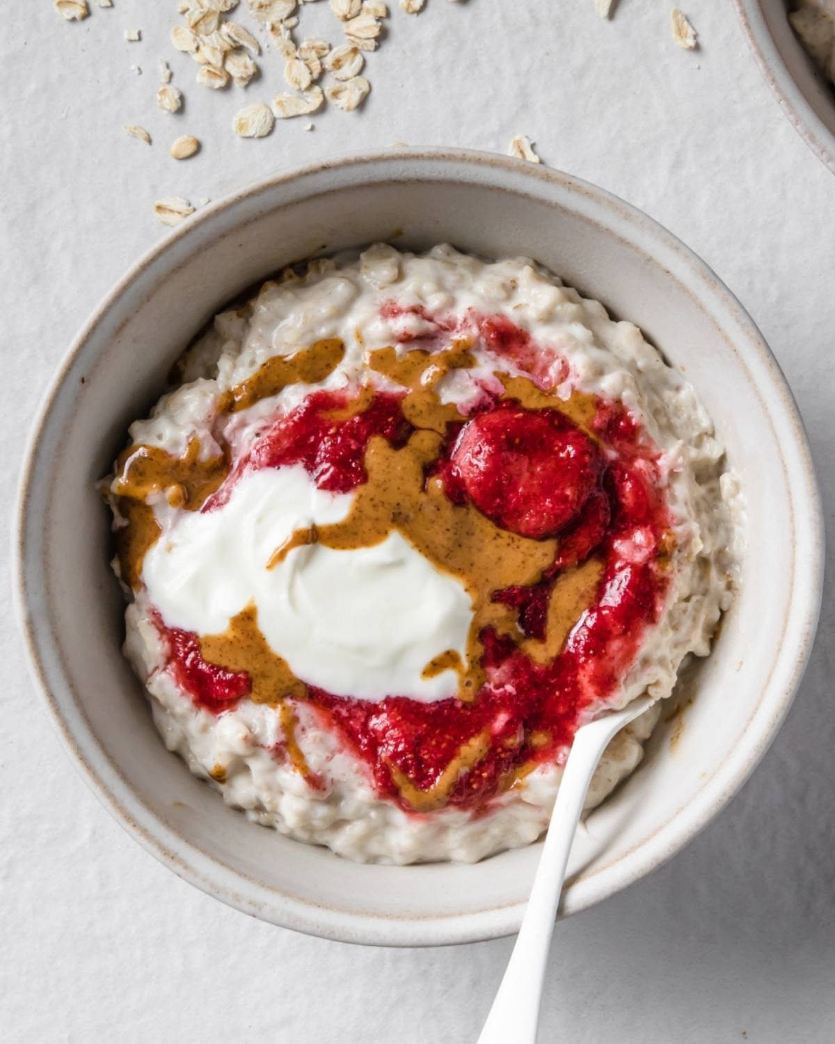 a bowl ot oatmeal toppd with yogurt, peanut butter, and strawberry jam