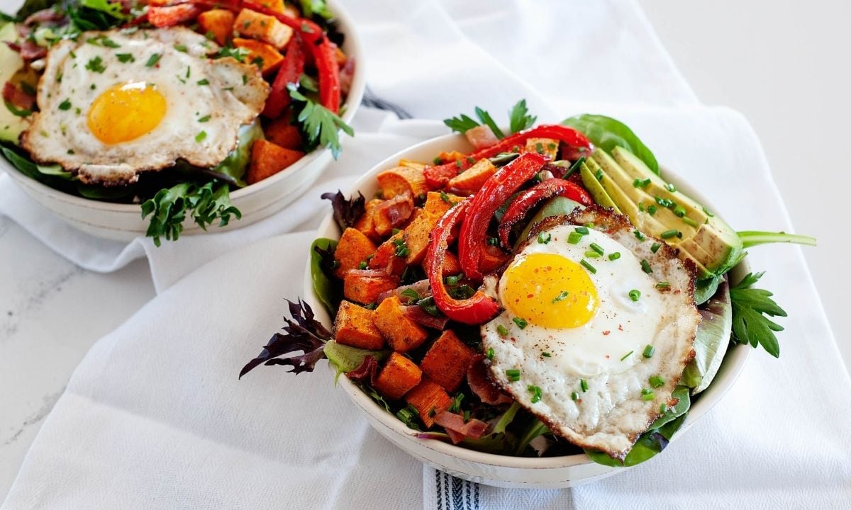 two bows of breakfast salad with avocado, sweet potatoes, bell pepper and a fried egg