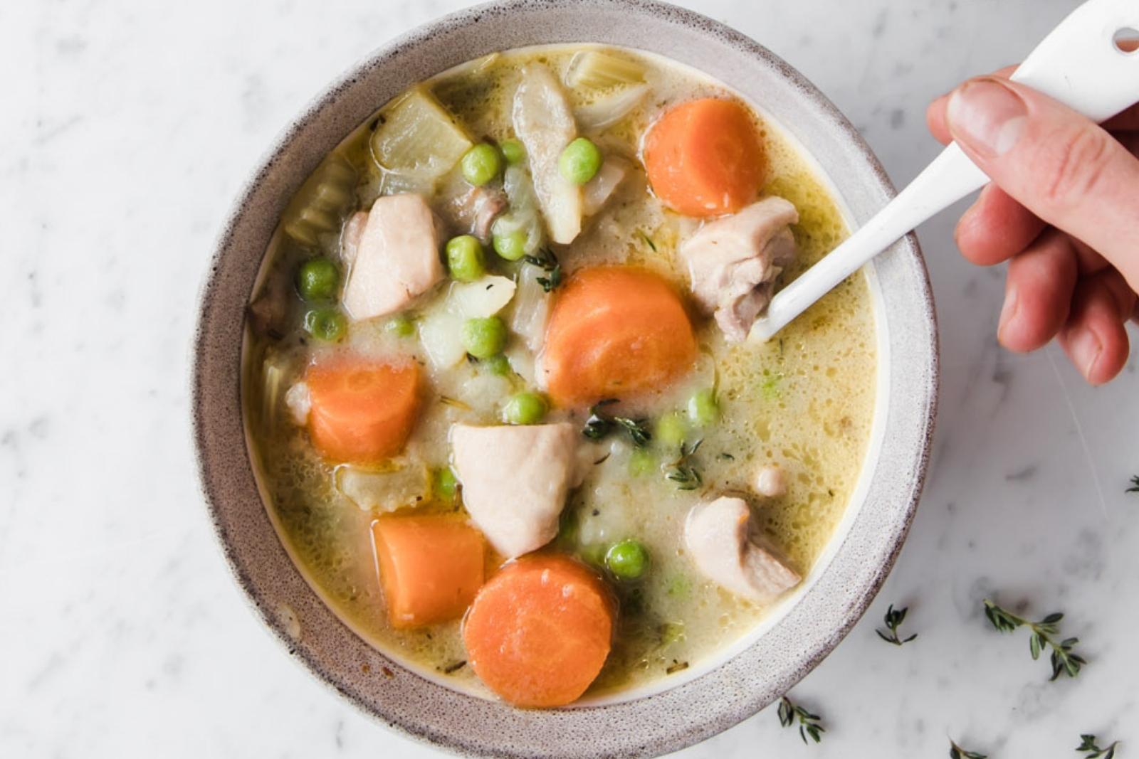 hand holding a spoon in a bowl of chicken stew