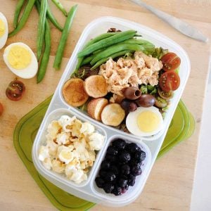salmon nicoise salad in a lunchbox with blueberries and popcorn