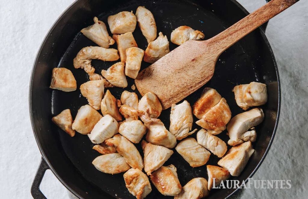 chicken pieces in a pan with a wooden spoon