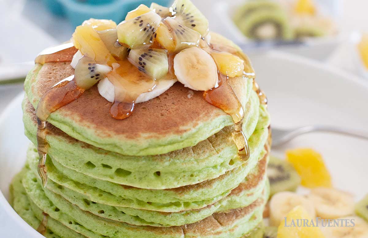 large stack of green spinach pancakes topped with kiwi and banana