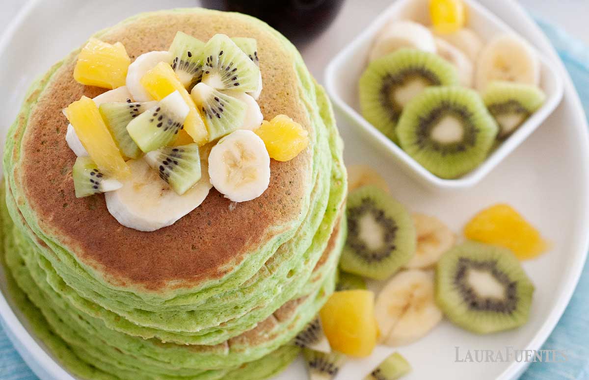 large stack of green pancakes topped with fruit and syrup