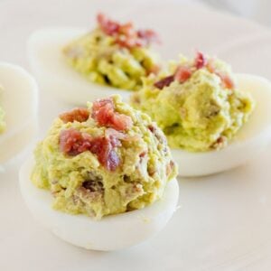 three avocado deviled eggs with bacon on a white dish