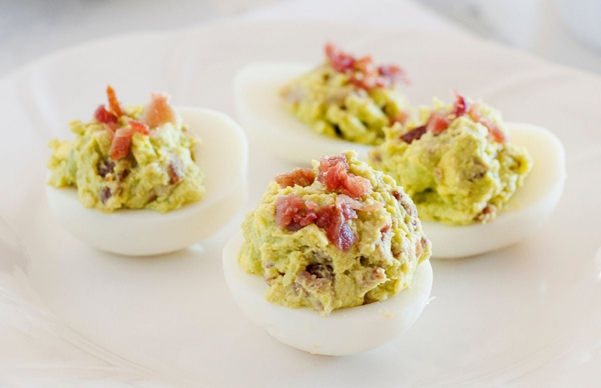 four avocado deviled eggs with bacon on a white dish
