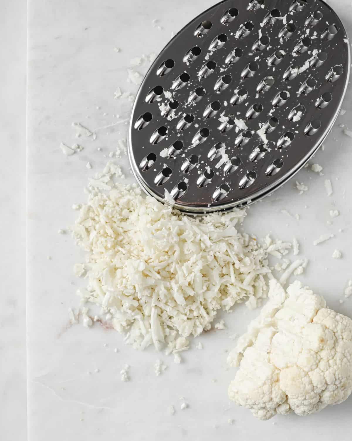 cauliflower rice, a cheese grater and a cauliflower chunk