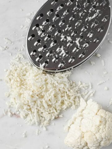 cauliflower rice, a cheese grater and a cauliflower chunk