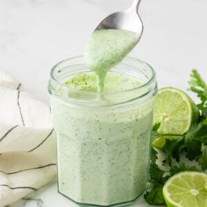 jar filled with homemade cilantro lime sauce and a spoon drizzling some sauce to show creamy texture