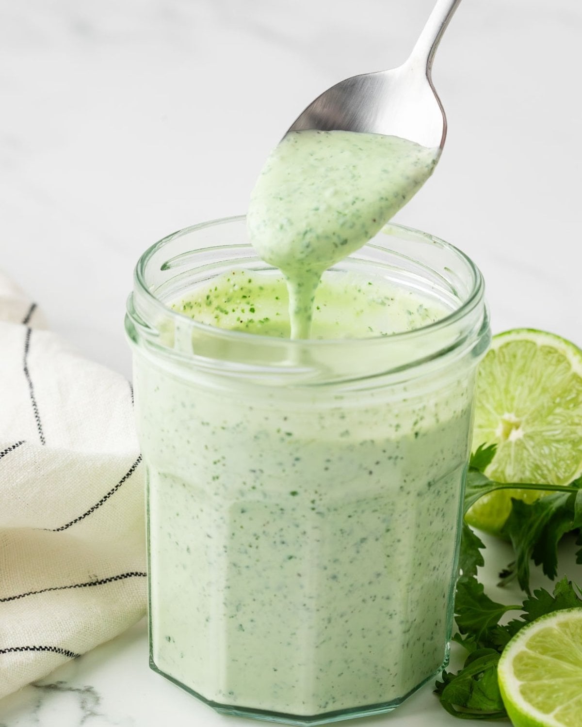 jar filled with homemade cilantro lime sauce and a spoon drizzling some sauce to show creamy texture
